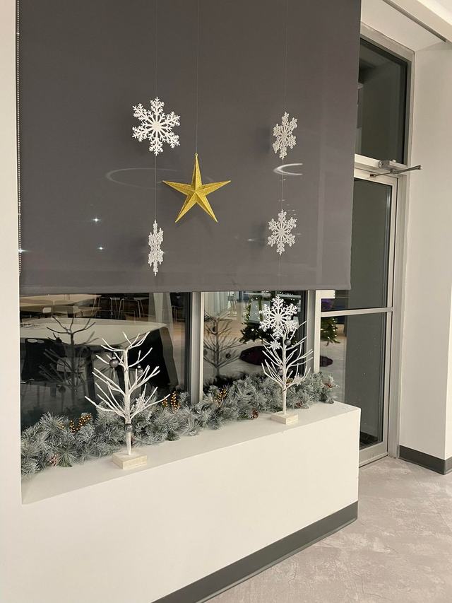 Frosted garland and white lit branches in a window planter with snowflake decorations