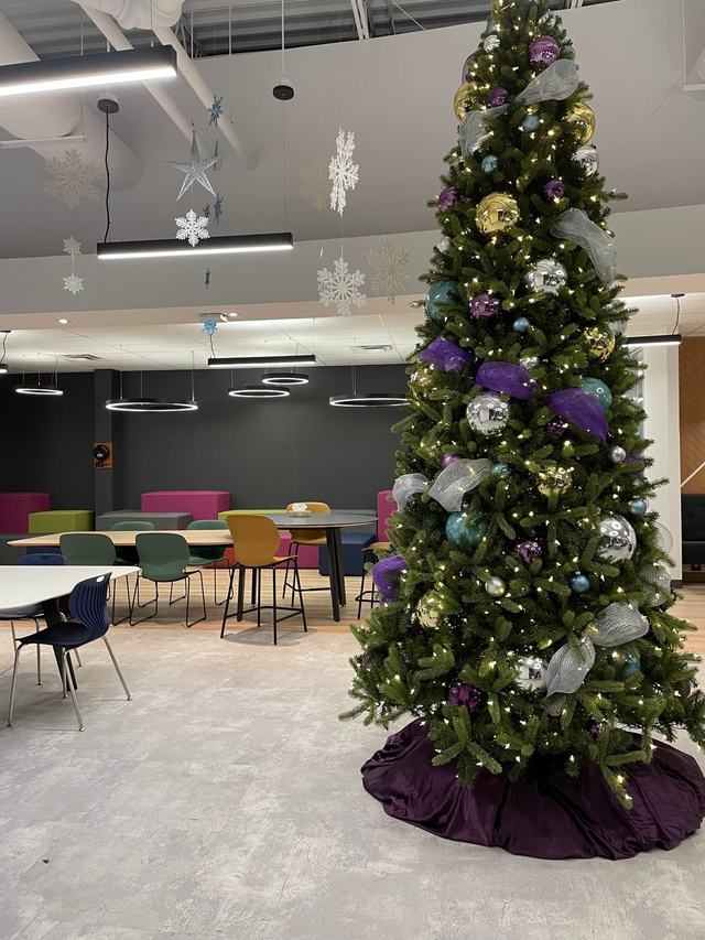 Tall Christmas tree with purple and silver baubles in a bright open-plan office
