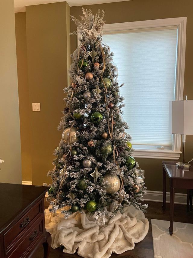 Flocked Christmas tree with green and gold baubles and a faux fur tree skirt