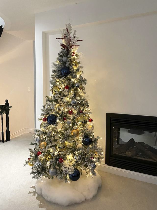 Flocked Christmas tree with navy, red and gold baubles beside a fireplace