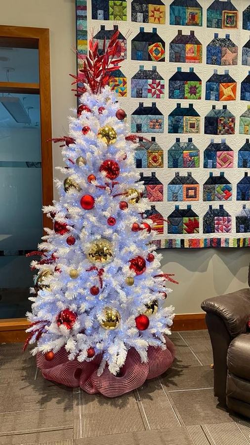 White Christmas tree with red and gold baubles in front of a patchwork quilt