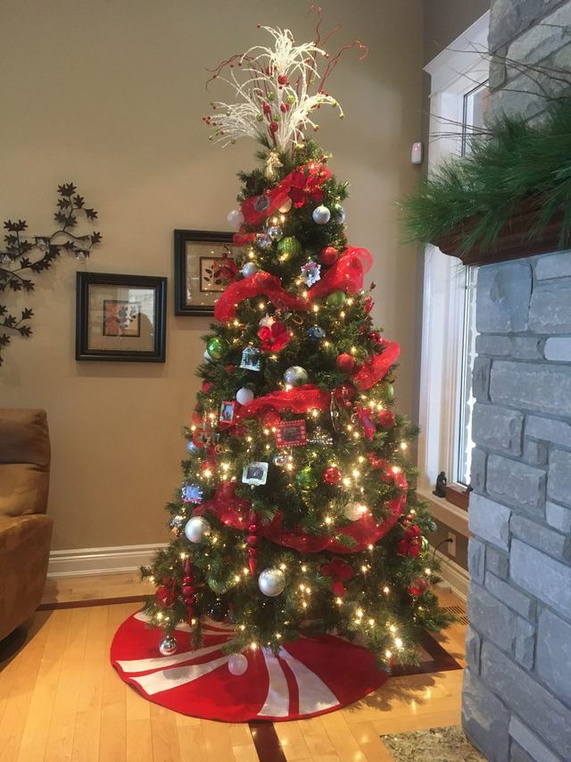 Red ribbon Christmas tree with a candy-stripe tree skirt beside a stone fireplace