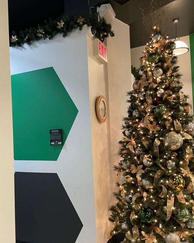 Christmas tree with gold ribbon and cream flowers beside a green feature wall