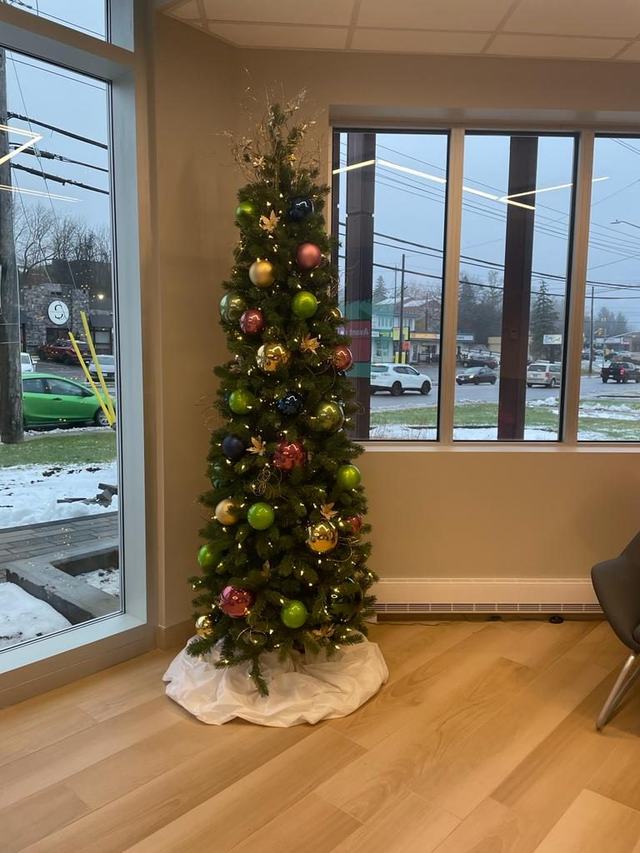 Slim pencil Christmas tree with green and gold baubles by a window