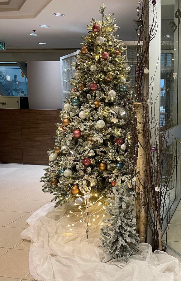 Flocked Christmas tree with gold and copper baubles beside birch branches in a lobby