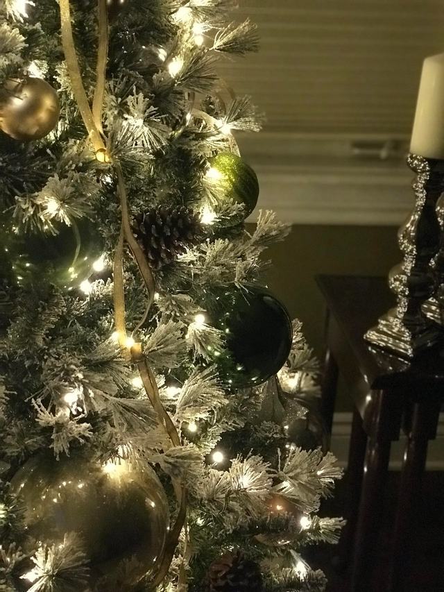 Close-up of a flocked Christmas tree with gold ribbon and green baubles