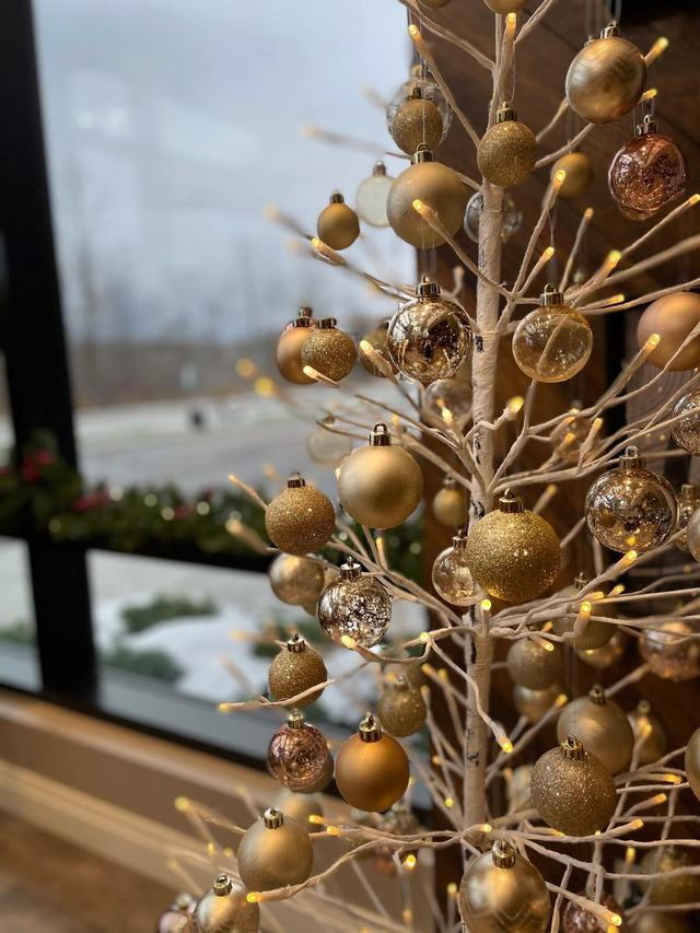 Gold baubles hung on a lit birch branch tree beside a window