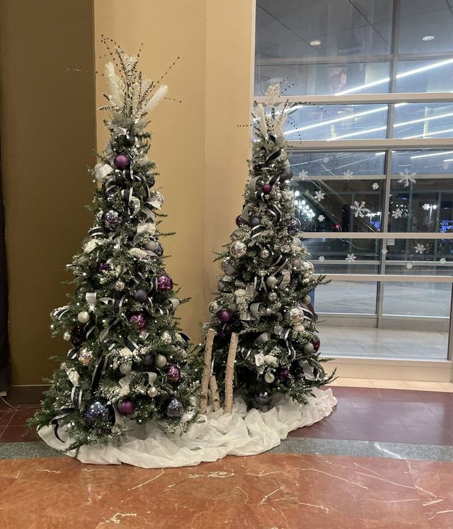 Two Christmas trees with purple and silver decorations on a marble floor