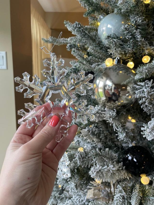 Hand holding a glass snowflake ornament against a flocked Christmas tree
