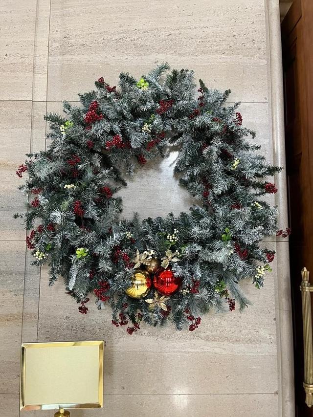 Flocked Christmas wreath with red berries and baubles on a stone wall